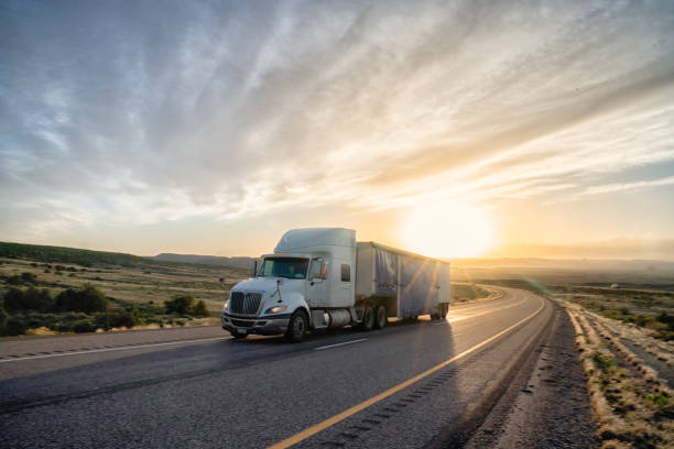 long haul semi truck rast down a four lane highway in a beautiful sunset - four lane highway stock-fotos und bilder