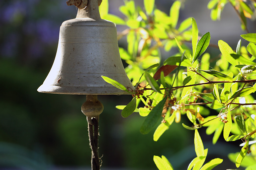 An old entrance bell in the courtyard against a green and yellow background of bush and sun