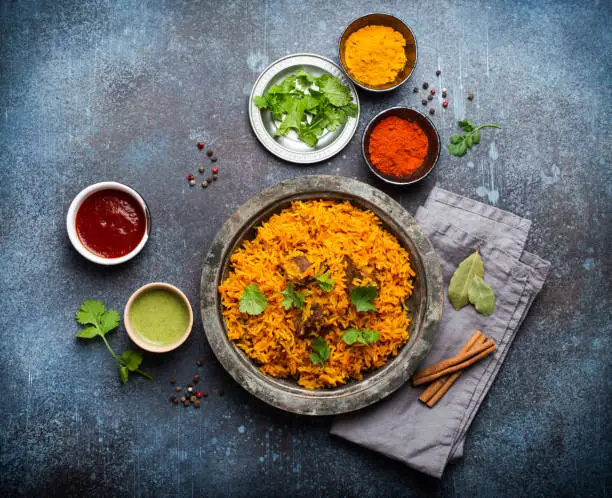 Pilaf - traditional Eastern/Asian dish made with rice, vegetables and meat served on vintage plate with fresh cilantro, sauces and spices on rustic background, top view, close-up