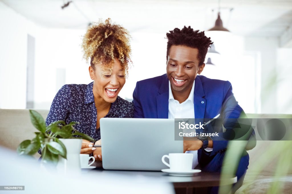 Happy professionals looking at laptop in office Happy professionals looking at laptop in office. Male and female corporate workers are planning business. They are wearing formals. African-American Ethnicity Stock Photo