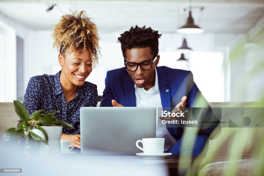 Mid adult colleagues discussing over laptop Mid adult businessman and businesswoman discussing over laptop. Financial advisors are planning business. They are surprised and happy. 30-34 Years Stock Photo