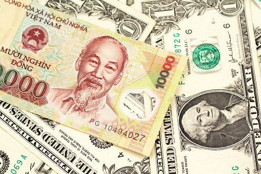A close up image of a Vietnamese ten thousand dong bank note on a background of one dollar bills in macro
