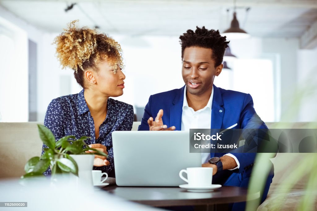 Businessman talking to businesswoman in office Businessman talking while working with businesswoman. Financial experts are planning business. They are sitting in office. Discussion Stock Photo