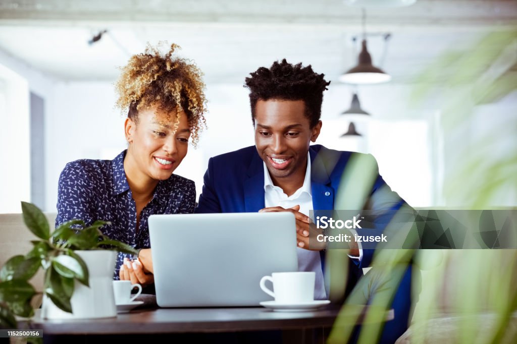Smiling white collar workers looking at laptop Confident smiling white collar workers looking at laptop. Coworkers are working on investment plans at work place. They are related to financial occupation. Financial Planning Stock Photo