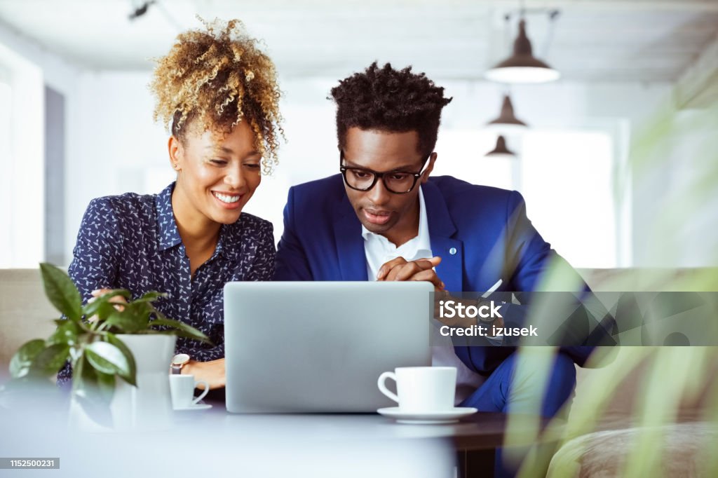 Confident white collar workers looking at laptop Confident white collar workers looking at laptop. Coworkers are working on investment plans at work place. They are related to financial occupation. Laptop Stock Photo
