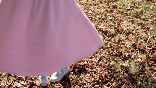 Close-up of a girl in pink skirt whirling in the dance at the autumn foliage, slow motion