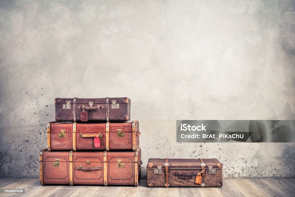 Vintage classic outdated trunks luggage with tags, old antique leather suitcases front textured aged concrete wall background. Travel baggage concept. Retro style filtered photo Suitcase Stock Photo