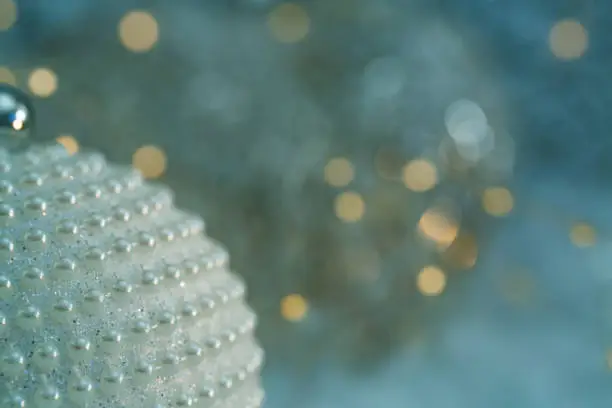 Christmas decoration. Ball with nacre pearls and beautiful blurred background of glittering bokeh with glowing lights. Greeting card. Happy Merry Christmas and New year. Toned image. Art photography.