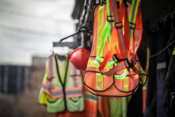 Personal protective equipments for sale on a shop: harness, reflective vests, yellow jackets, construction site helmets, as well as various other PPE devices Picture of PPE, or personal protective devices, for sale in a shop, haning. Yellow and Orange vests, harnesses and helmets are visible protective workwear stock pictures, royalty-free photos & images