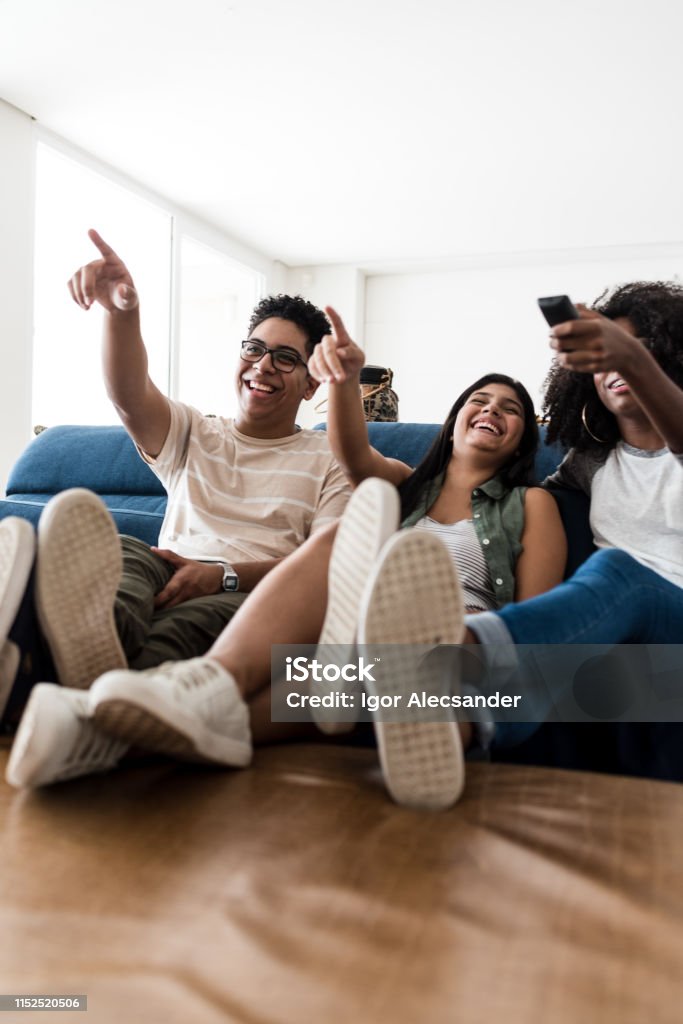 Adolescentes que sentam-se no sofá que escolhe o filme junto - Foto de stock de Assistir TV royalty-free