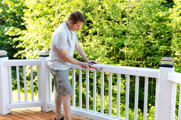 Mature man hammering nail into white railing of outdoor deck stock photo
