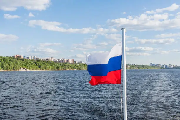 Flag of Russia develops in the wind against the background of the city and the river