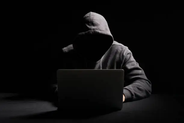 Unrecognisable person working on laptop in the dark. Concept of hacking data.