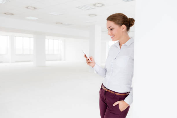 Smiling young businesswoman using smartphone while standing at new empty office