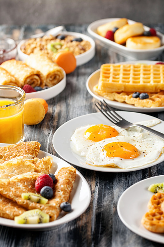 Breakfast - fried eggs, pancakes, crepes, croissants, wafers, a granola on a wooden background.