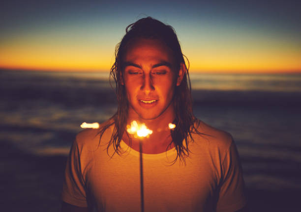 Shot of a young man holding a sparkler at the beach at night