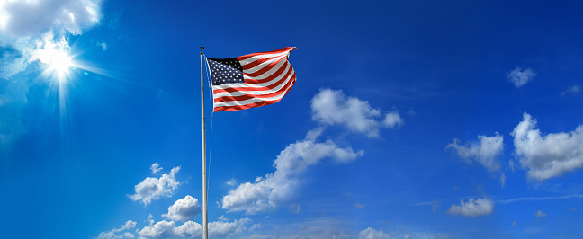 Conceptual image of waving American flag hanged at tall pole over clear blue sky