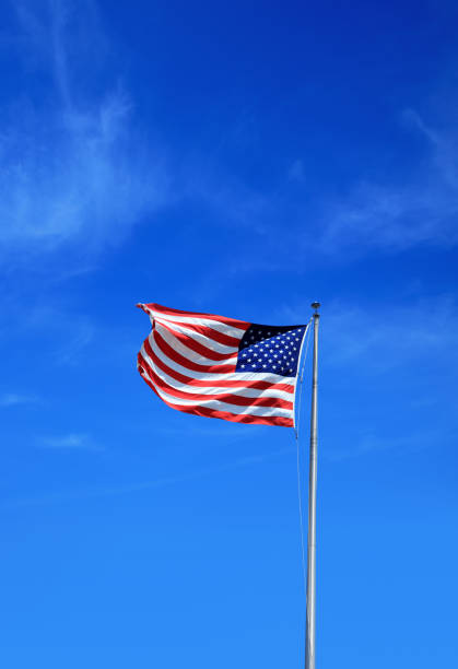 istock waving American flag tall flagpole over sunny blue sky 1152565899