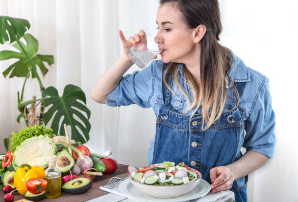 istock Young woman drinking water at the table with vegetables 1152567472