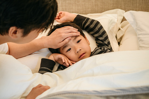 Sick child lying in bed, father reassuring and consoling, healthcare, medicine, care