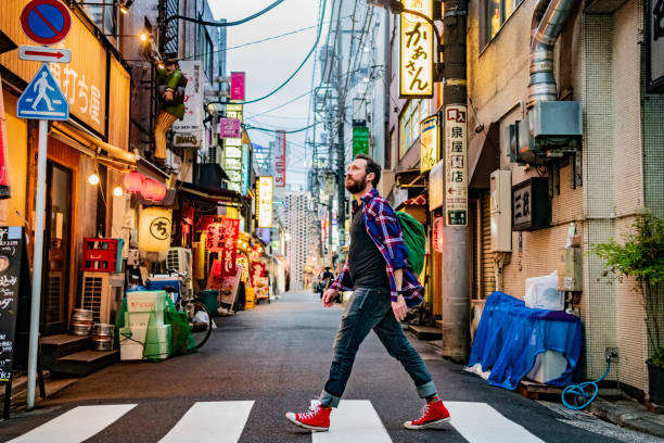Portrait of man walking on zebra crossing on Tokyo street Backpacker crossing road on urban street, sight seeing, exploration, cool offbeat stock pictures, royalty-free photos & images