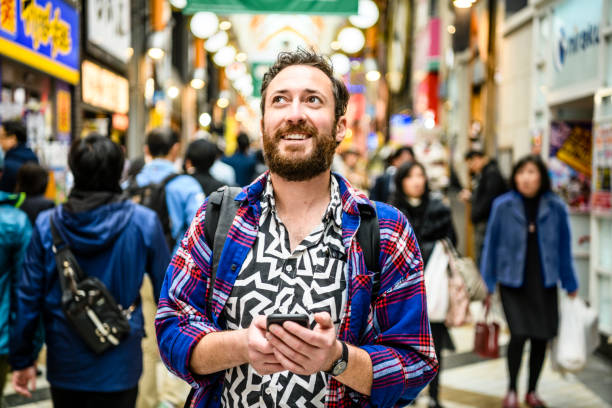Portrait of tourist in patterned shirt looking up on busy street Mid adult man using smartphone to navigate, excitement, sight seeing, awe male meaning stock pictures, royalty-free photos & images