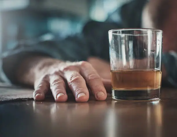 Photo of Hand by glass of liquor, man's head on table
