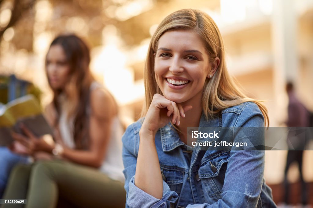 I'm extremely proud to be postgrad Cropped portrait of an attractive young female student siting outdoors on campus with her classmates in the background University Stock Photo