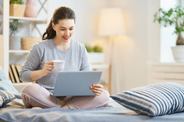 femme travaillant sur un ordinateur portatif - using computer bedroom one woman only cheerful photos et images de collection