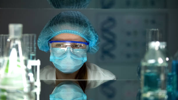 istock Lab worker in protective eyeglasses and uniform looking at chemical reagents 1152598054