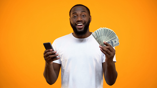Excited Afro-American man holding smartphone and dollars, online money transfer