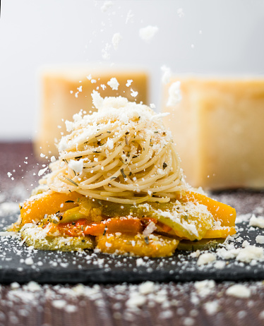 Falling cheese on a freshly prepared spaghetti pasta with vegetables. Fresh Piece of Cheese on background