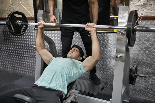 Young man practicing bench press at health club. Male is exercising in gym. He is lying on weight bench.