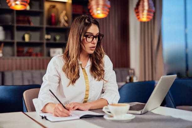istock Woman taking notes in agenda and looking at laptop while sitting in cafe. 1152601197
