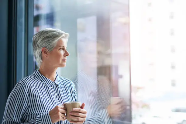 Shot of an attractive mature businesswoman drinking coffee while looking out of her office window