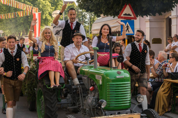 Riding the tractor Villach, Austria - August 4th, 2018: Participants riding a tractor at the procession of 'Villacher Kirchtag', the largest traditional folk festival in Austria, at its 75th occurence. villach stock pictures, royalty-free photos & images