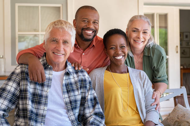 Group of multiethnic mature friends portrait Senior couple with mature man and african woman posing for a photo sitting at courtyard. Portrait of happy multiethnic people sitting on couch under patio. Cheerful men and beautiful women looking at camera. happiness four people cheerful senior adult stock pictures, royalty-free photos & images