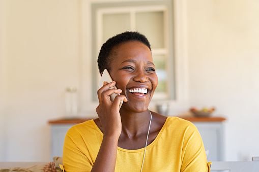 Smiling african american woman talking on the phone. Mature black woman in conversation using mobile phone while laughing. Young cheerful lady having fun during a funny conversation call.