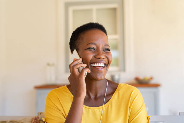 Woman laughing while talking on phone Smiling african american woman talking on the phone. Mature black woman in conversation using mobile phone while laughing. Young cheerful lady having fun during a funny conversation call. gossip photos stock pictures, royalty-free photos & images
