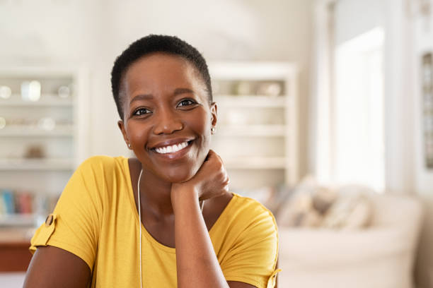 Cheerful mature black woman Portrait of mature woman sitting at home and looking at camera. Cheerful black girl with short hair in casual sitting in her new apartment with copy space. Satisfied woman smiling while looking at camera. beautiful older black woman stock pictures, royalty-free photos & images