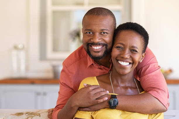 Cheerful mature balck couple Happy mature black couple bonding to each other and smiling while sitting on couch. Portrait of smiling black man embrace his wife from behind and looking at camera. Smiling husband and beautiful woman laughing. african american couple stock pictures, royalty-free photos & images