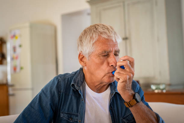 Senior man using asthma pump Senior man using asthma inhaler for relief an attack at home. Old man using asthma inhaler for preventing attack. Mature man using medical inhaler to prevent and treat wheezing and shortness of breath caused by allergy. air attack photos stock pictures, royalty-free photos & images