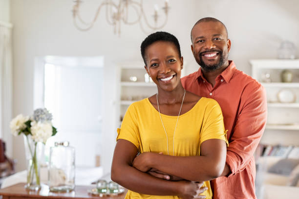 Mature black couple hugging and smiling Smiling mature couple holding each other at home. Loving african couple standing in living room embracing and looking at camera. Husband hugging wife from stomach at new apartment with copy space. african american couple stock pictures, royalty-free photos & images
