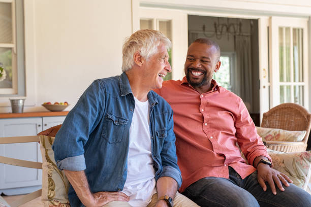 Happy men in a conversation Two friends talking while sitting on couch in the courtyard. Senior man and african guy laughing while in conversation sitting outside home. Two men talking to each other and enjoying. male friendship stock pictures, royalty-free photos & images