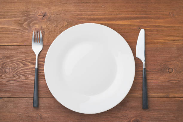 istock clean empty white plate, fork and knife on brown wooden table, copy space, mock up, top view. 1152606592