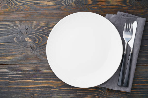 istock clean empty white plate, fork and knife on dark rustic wooden table, copy space, mock up, top view. 1152606685