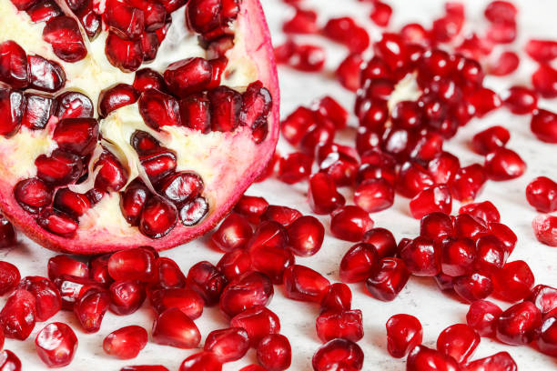 istock Halved pomegranate with gem like fruit seeds scattered near on white working board. 1152609543