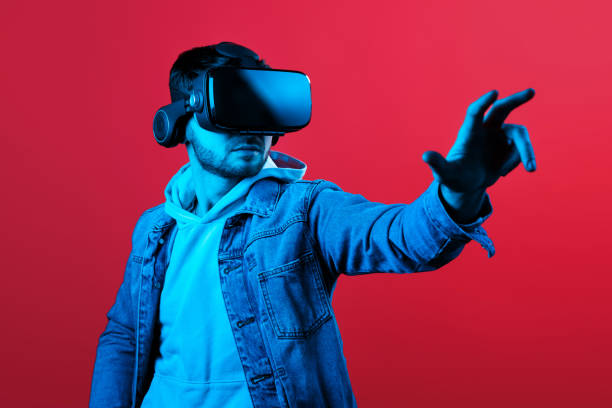 istock Attractive bearded man trying VR headset and exploring another world in studio on red background in neon light. Smartphone using with VR headset. 1152611731