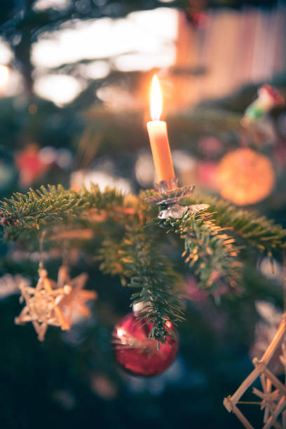 istock Candle on traditional decorated Christmas tree, evening. People in the blurry background. 1152612775