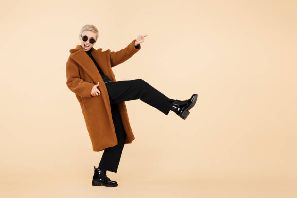 Attractive young hipster woman with blonde short hair wearing a coat and sunglasses play on invisible guitar isolated over beige background. Full lengh photo. Attractive young hipster woman with blonde short hair wearing a coat and sunglasses play on invisible guitar isolated over beige background. Full lengh photo crazy promotion stock pictures, royalty-free photos & images